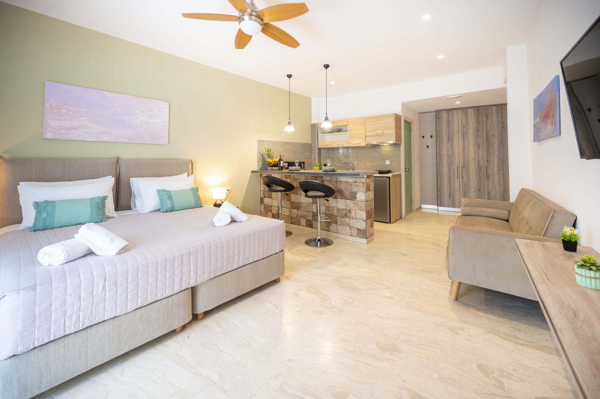 Monolocale luminoso con letto allestito come matrimoniale, quadro rosa, bancone bar e divano in velluto
